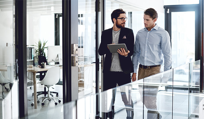 Two men walking in office viewing tablet 